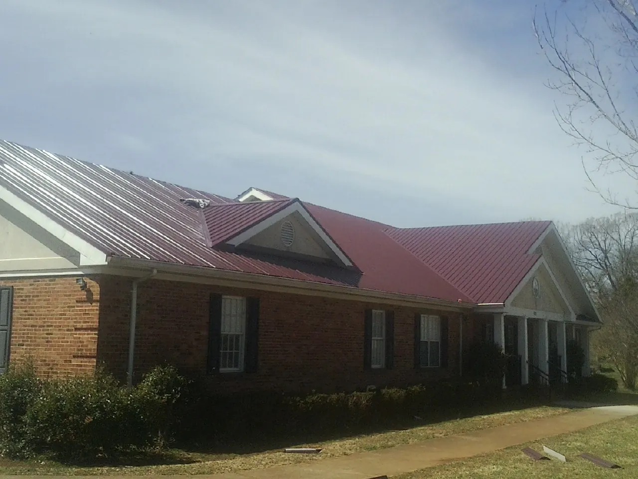 Red metal roof with gabled entries on a long brick building, from a Hail Damage Roof Repair job in Fort Hood