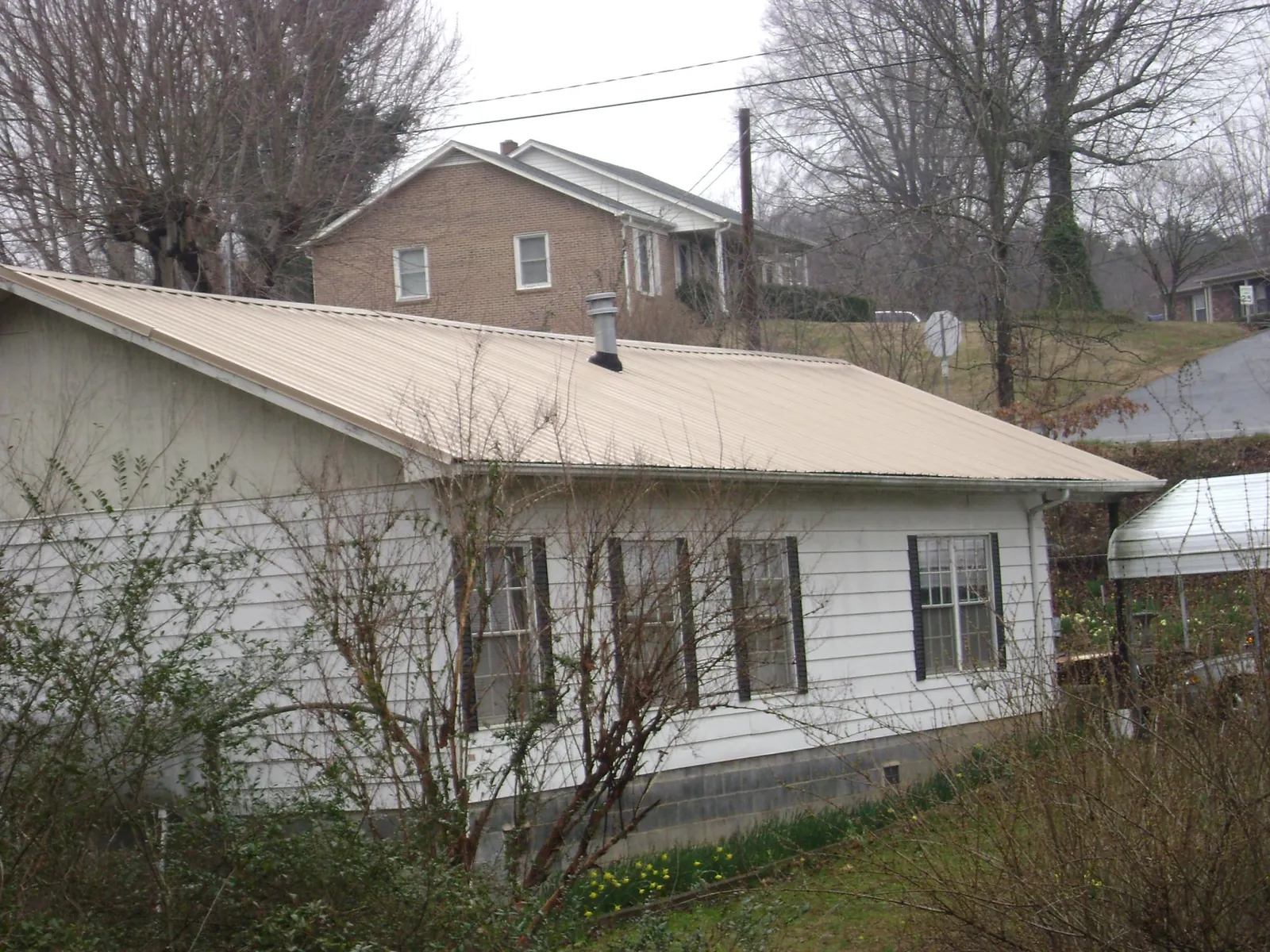 Tan metal roof on a white sided house set into a hillside — Commercial Roofing by Roofing Brothers in Fort Hood